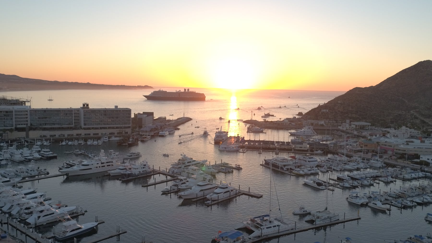 Sunrise casting warm light over boats and buildings in Cabo San Lucas marina.